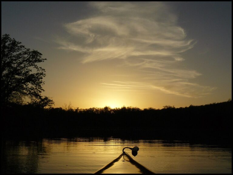 Kayaker paddling across a wide river at sunset
